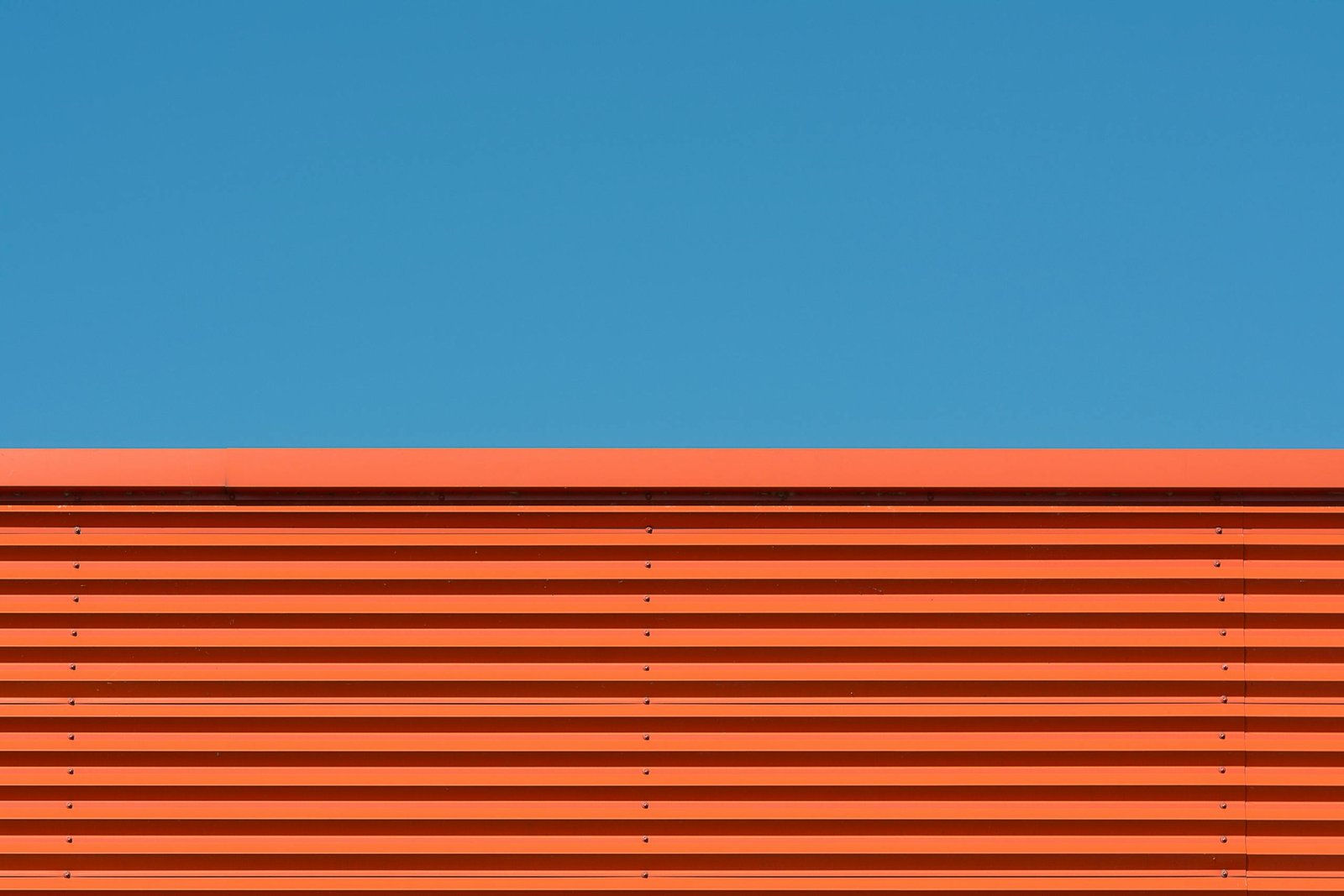A minimalist image featuring a vibrant orange wall and clear blue sky, showcasing simplicity and modern design.